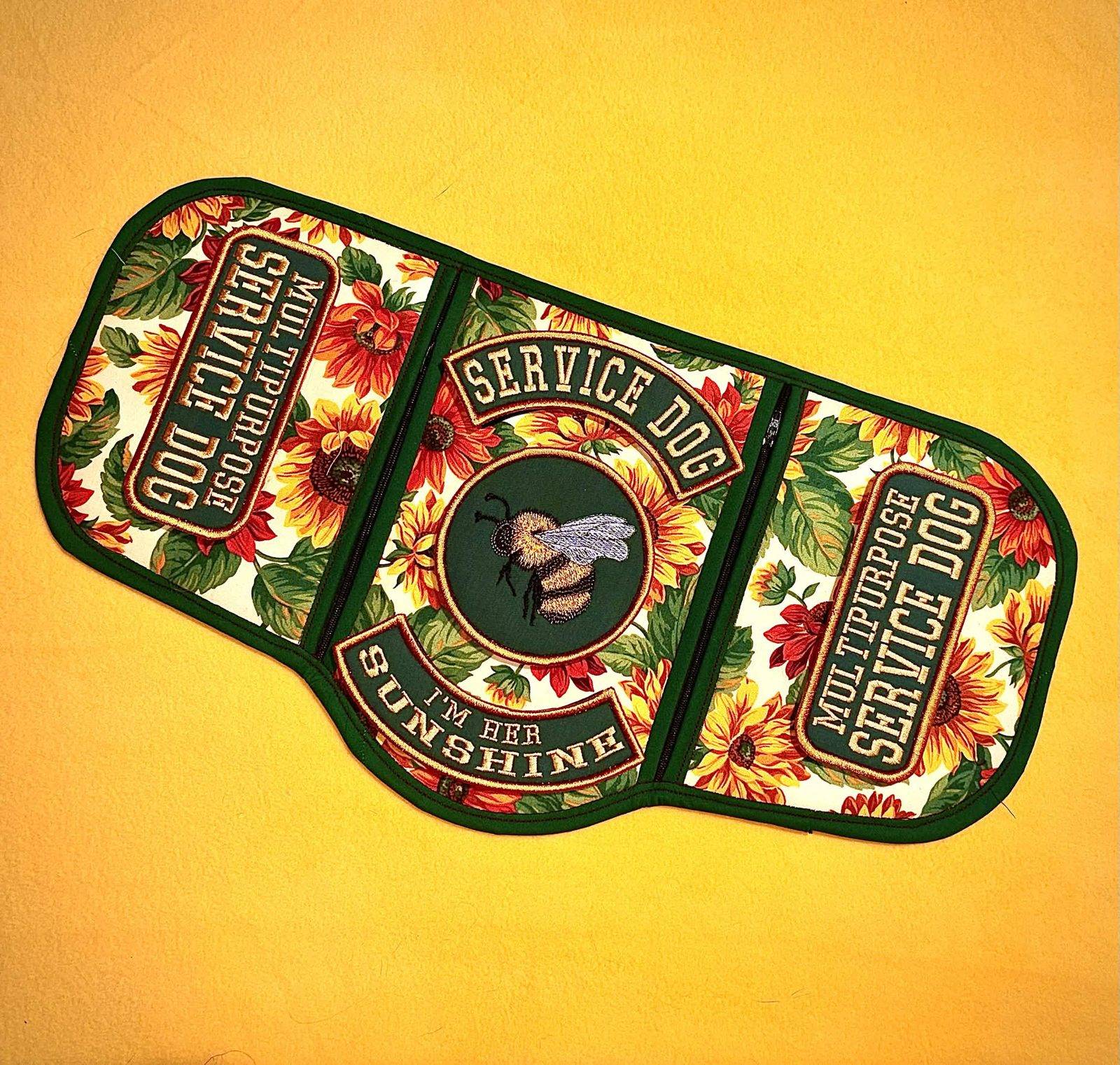 Sunflower-print three-panel service piece with dark green binding, an embroidered bumblebee in a badge reading Service Dog, I'm her sunshine, and Multipurpose Service Dog patches on both sides.