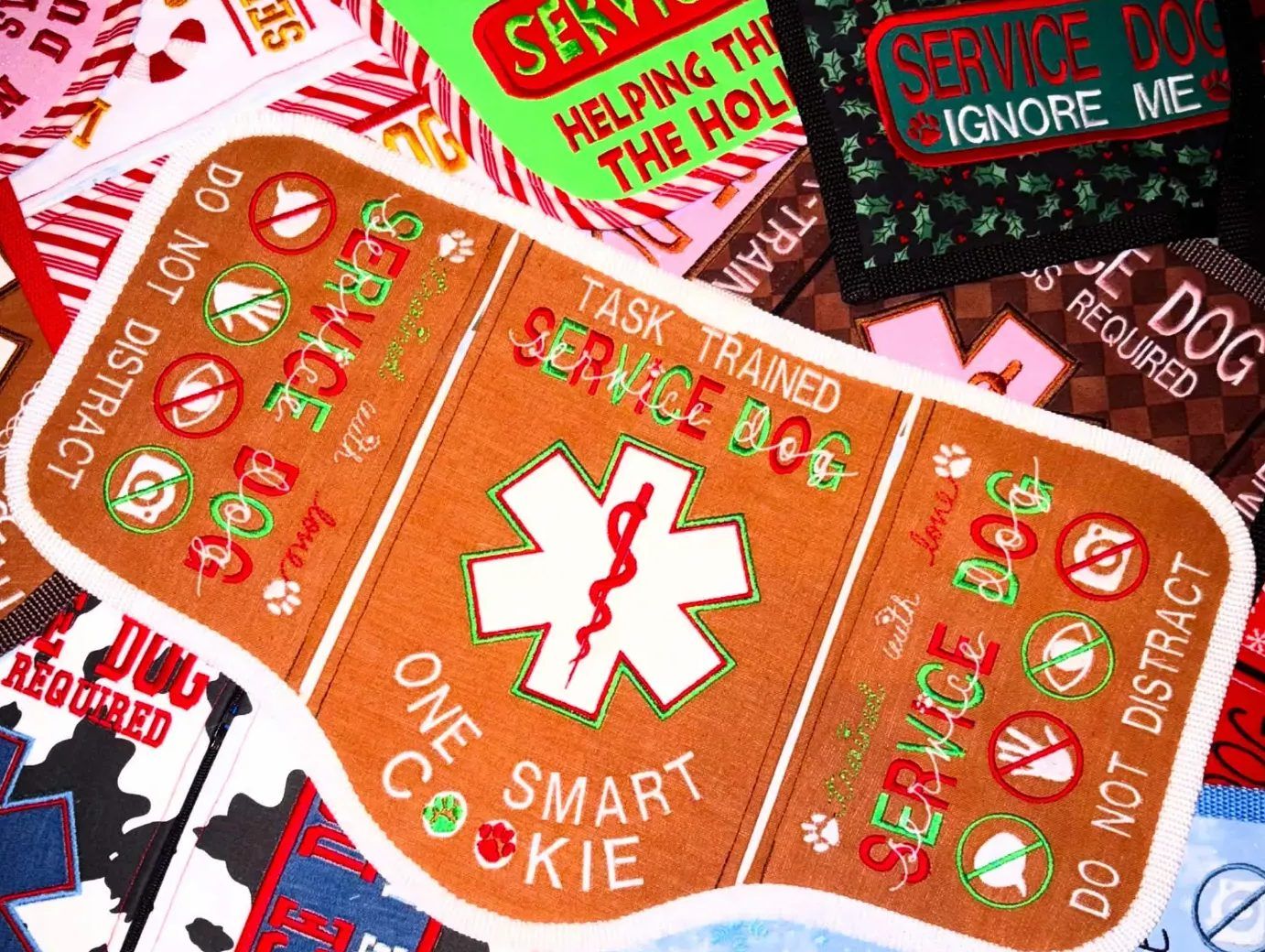 Gingerbread-coloured service vest reading Task trained service dog, One smart cookie, on a pile of holiday vests.