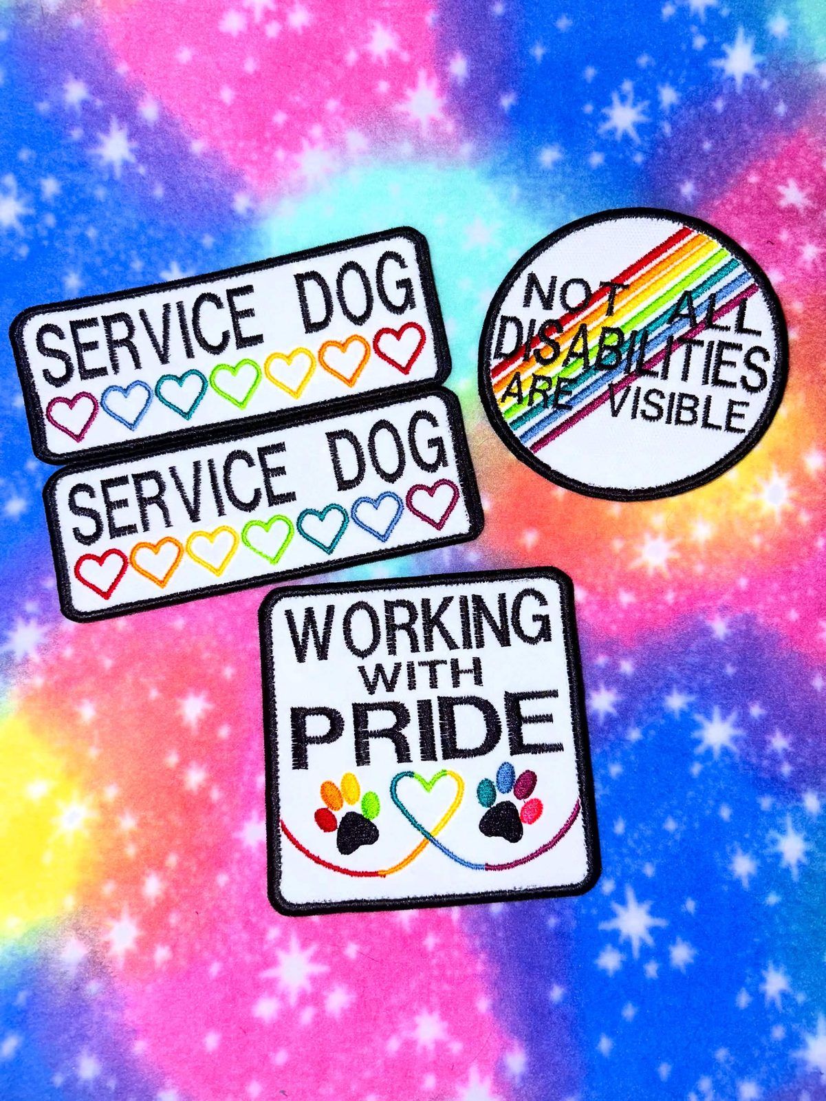 Embroidered patches on rainbow fabric: Service Dog with rainbow hearts, Working with Pride, and Not all disabilities are visible.